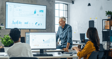 SaaS founder talking to employees in office beside KPI screen