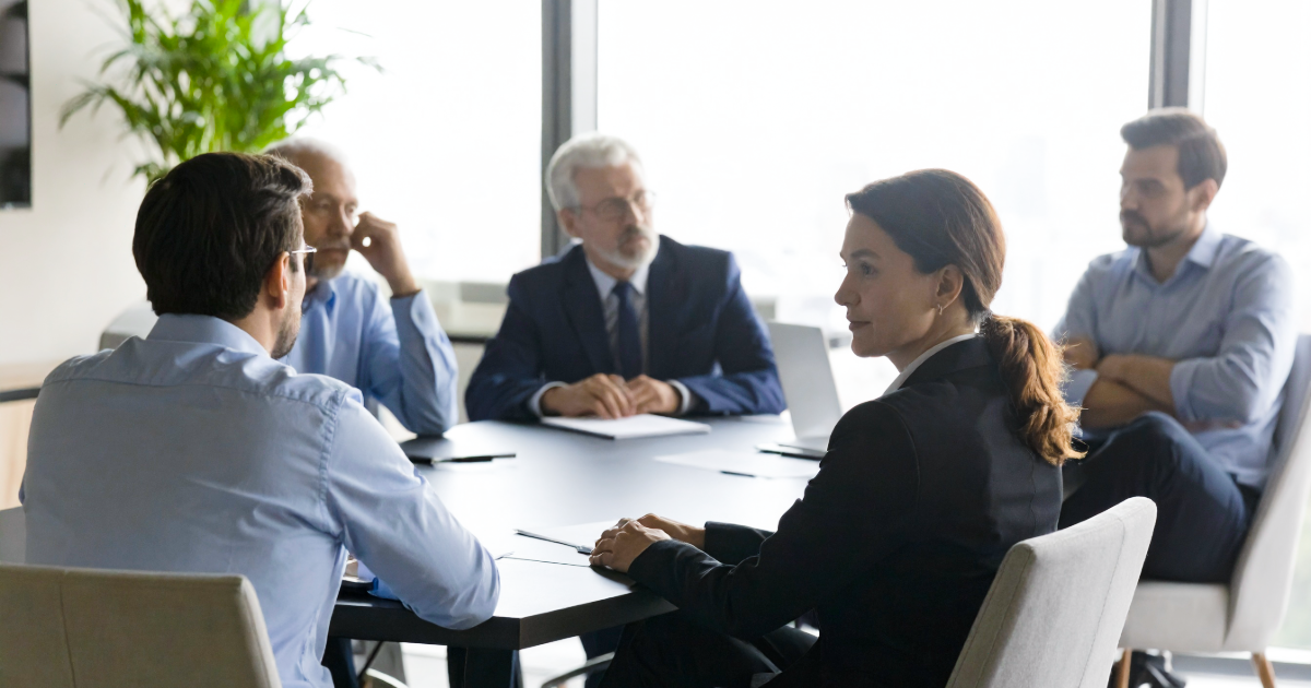 Corporate lawyer mediating a tense boardroom meeting between shareholders around a teak table before a business sale