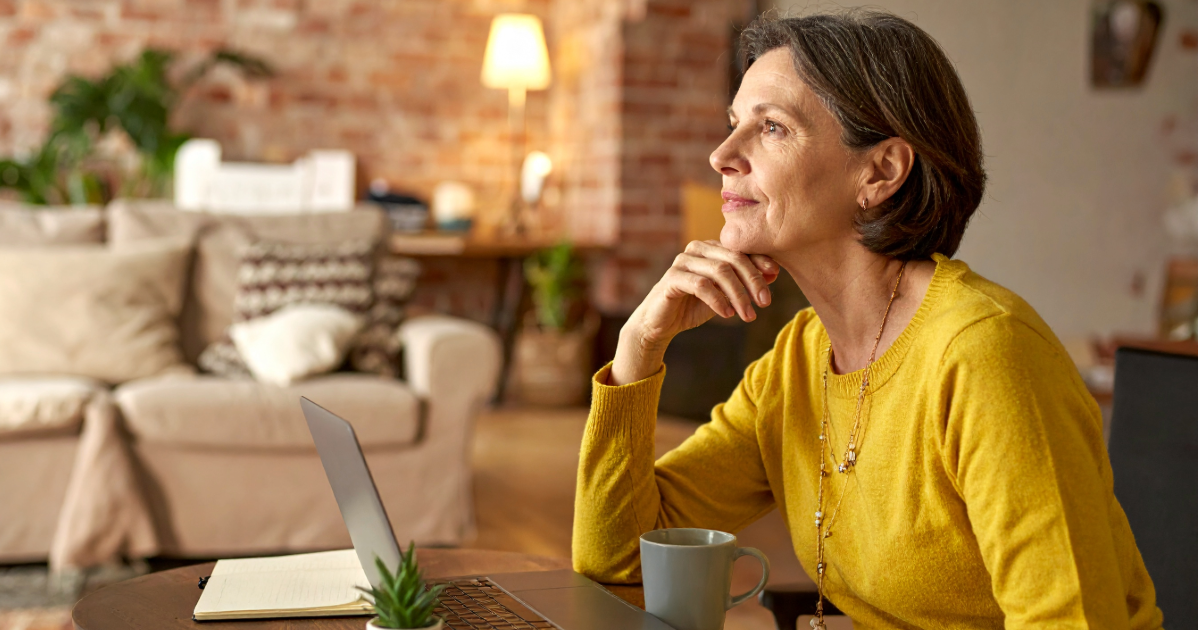 A founder in her late 50s sits in a softly lit, informal workspace, looking thoughtfully into the middle distance as she considers the timeline of selling her business.