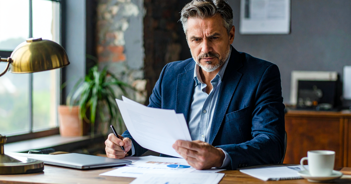 A founder of a regional engineering consultancy reviewing financial statements at his desk, considering what his business is worth.